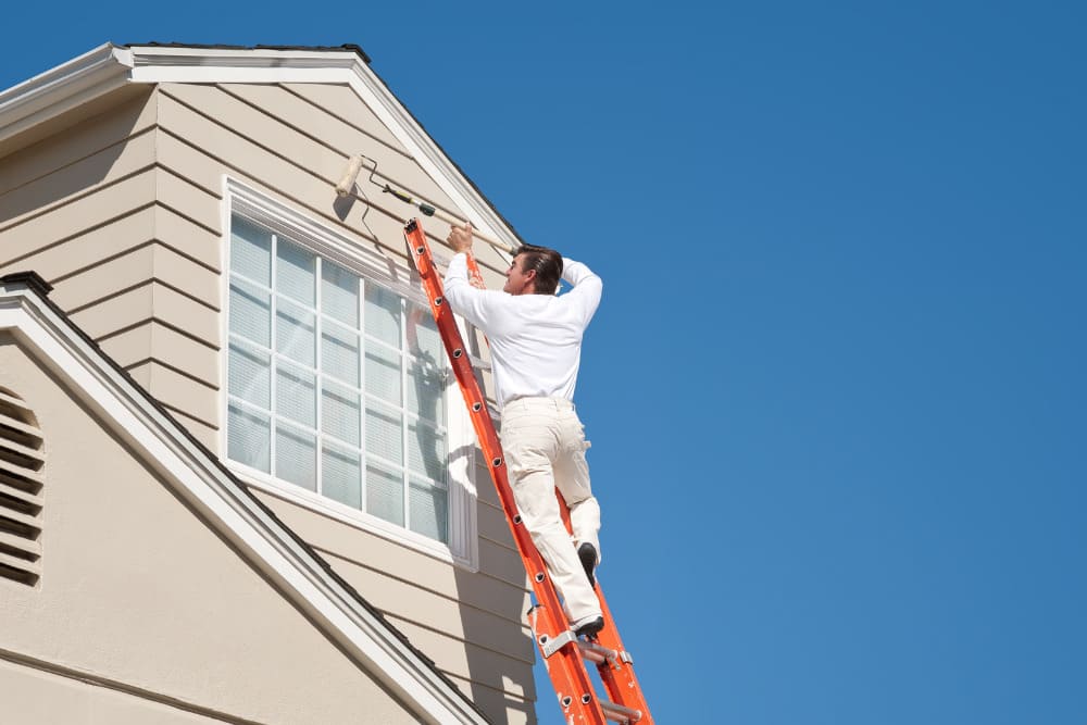 Professional painter on ladder painting home exterior